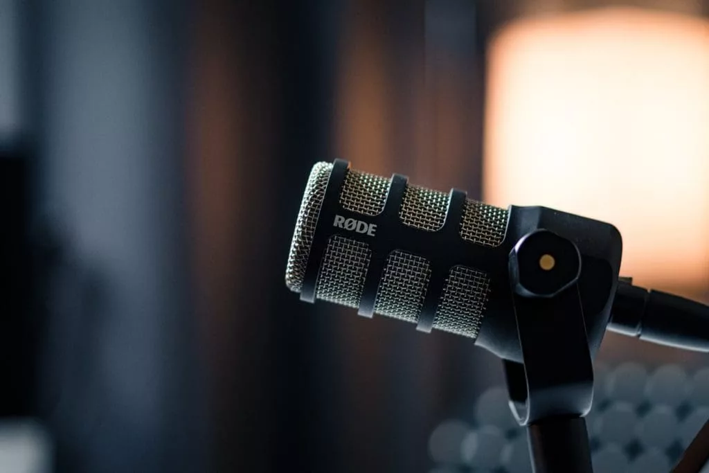 the rode podmic with a blurred out background. the mic is black with a gold grille.