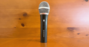 The audio-technica atr2100x USB microphone standing up on a wooden brown desk.